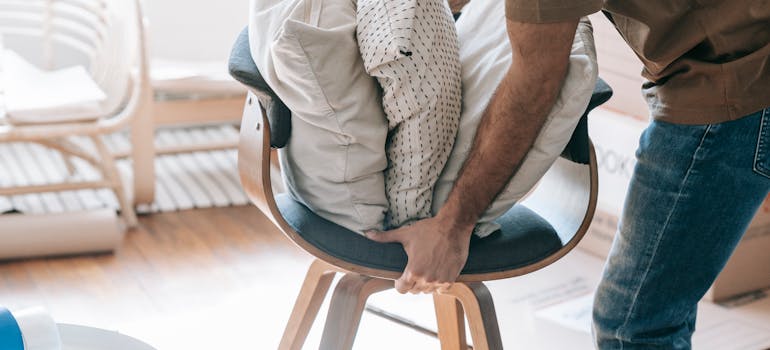 A person carrying a chair with throw pillows.