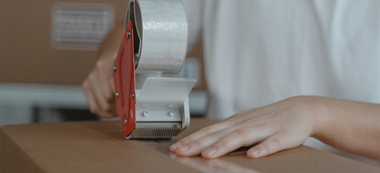A person sealing a box with packing tape.