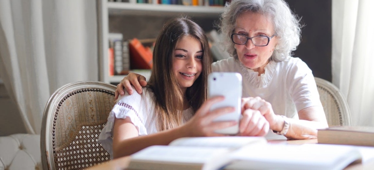 A woman and her granddaughter smiling while video calling someone.
