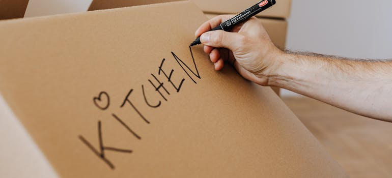 A person labeling a moving box before relocating kitchen essentials stress-free.
