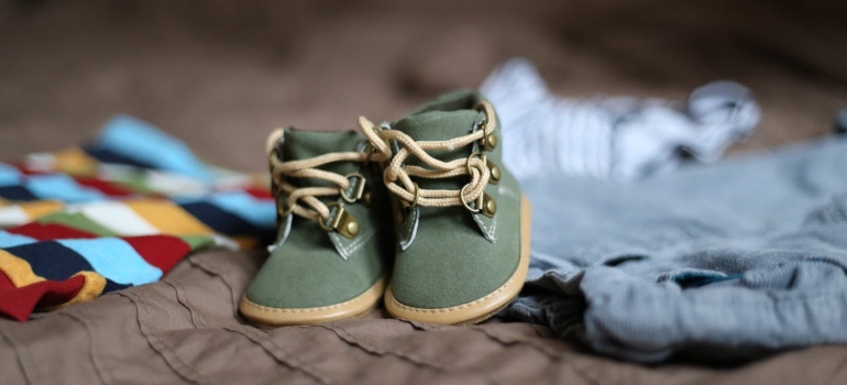 Baby shoes and clothes on a bed.