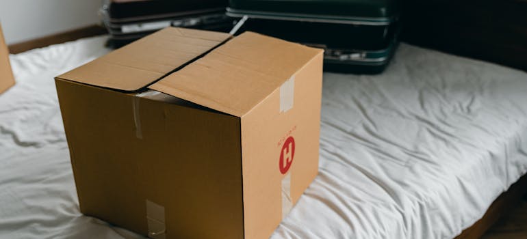 A moving box and suitcases on a bed.