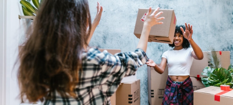 One person tossing a moving box to another.